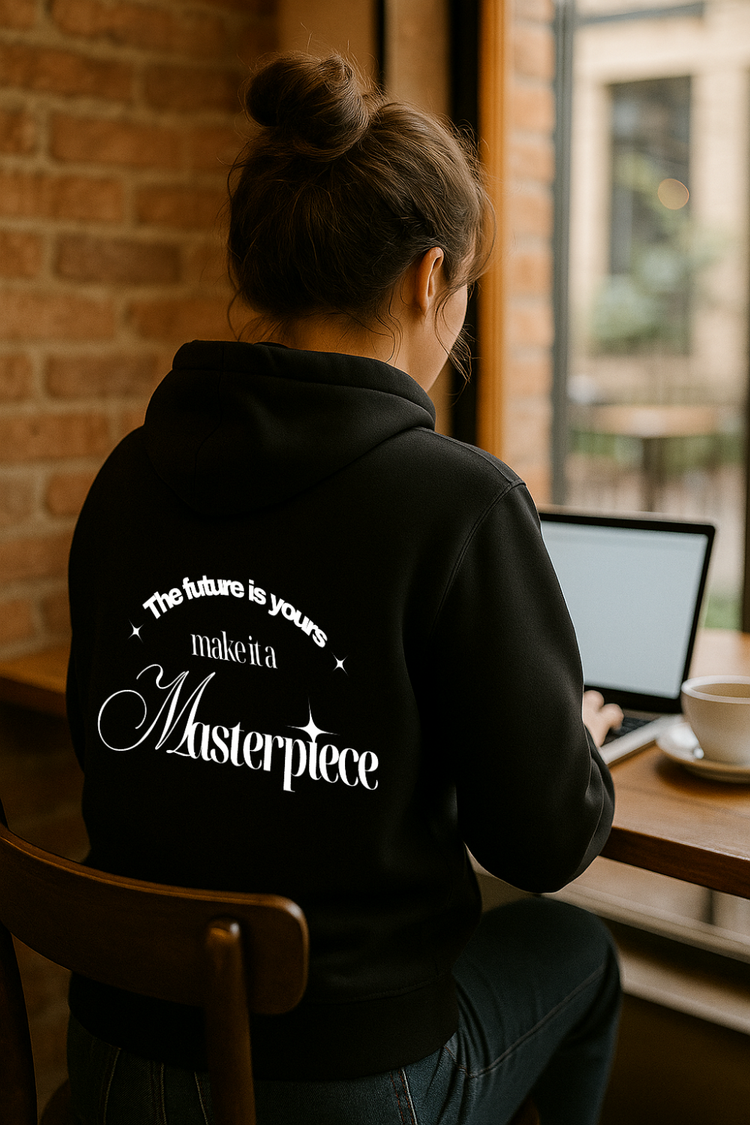 Frau mit Dutt sitzt im Café am Laptop und trägt schwarzen Zipper mit weißem Print "The future is yours - make it a Masterpiece" auf dem Rücken. Motivierendes Streetwear-Statement